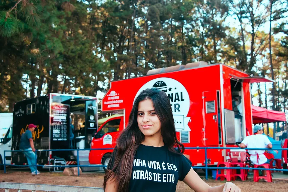 Ciemnowłosa kobieta stojąca w lesie przy barierce, w tle food trucki