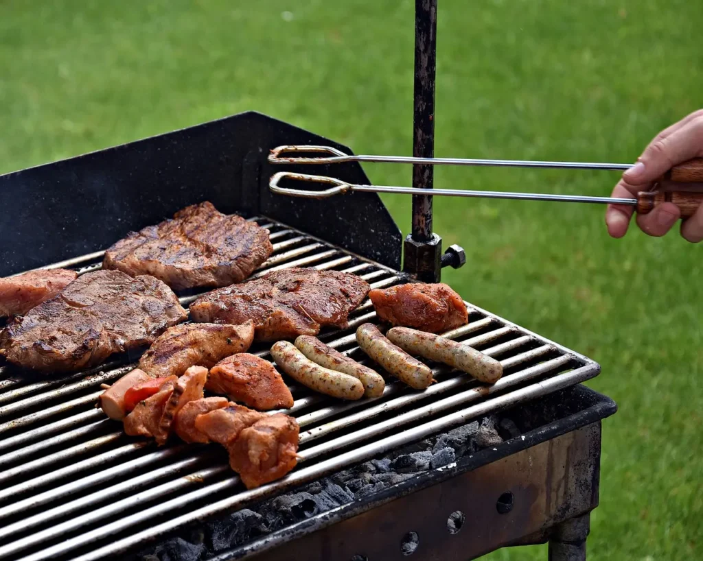 Mięso smażące się na grillu oraz ręce trzymające szczypce