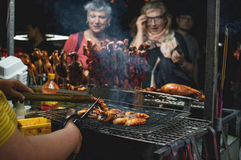 kiełbasy smażące się na grillu, w tle zaskoczone kobiety w starszym wieku